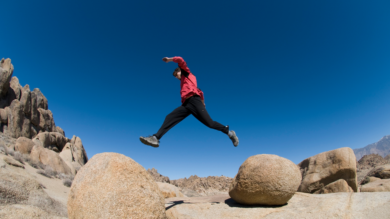Person leaping between two boulders, symbolising the closing of the gap between AI activity and value
